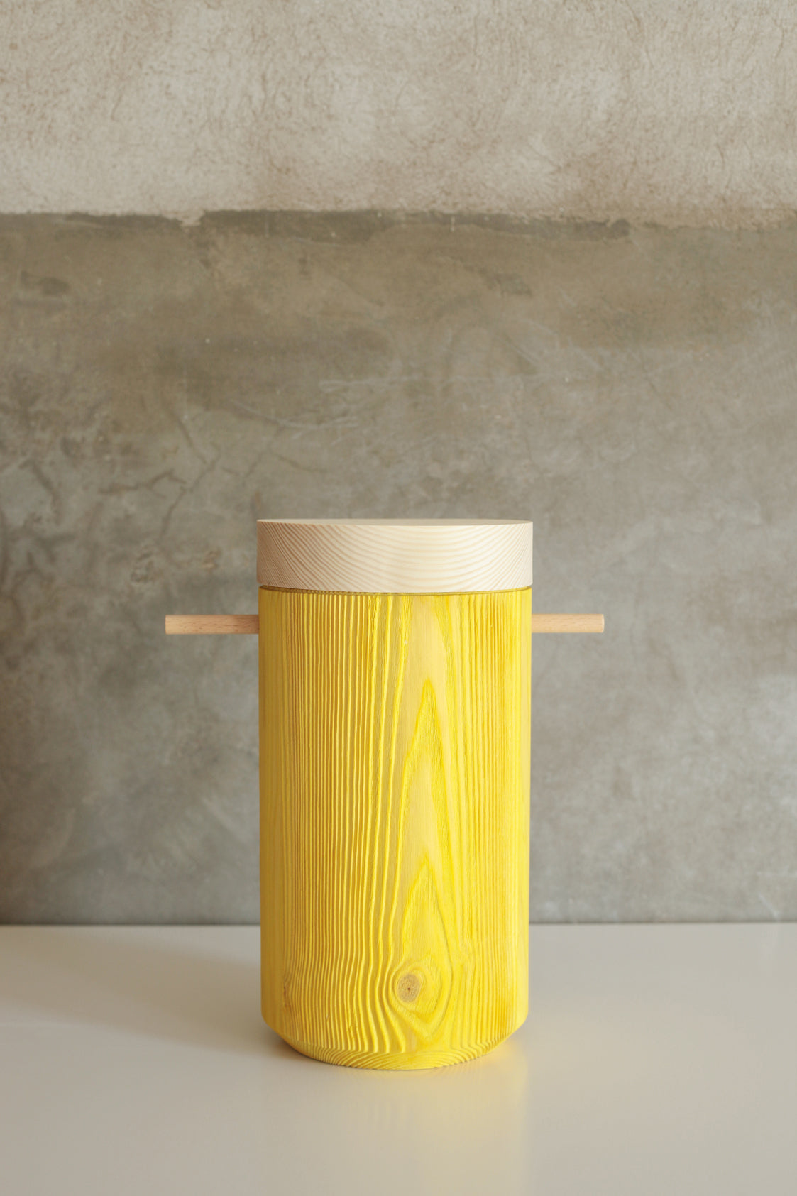 Bright yellow colored wooden urn displays on a white table