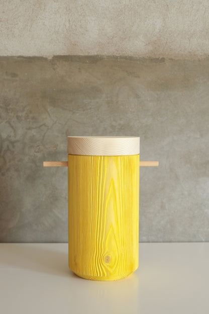 Bright yellow colored wooden urn displays on a white table