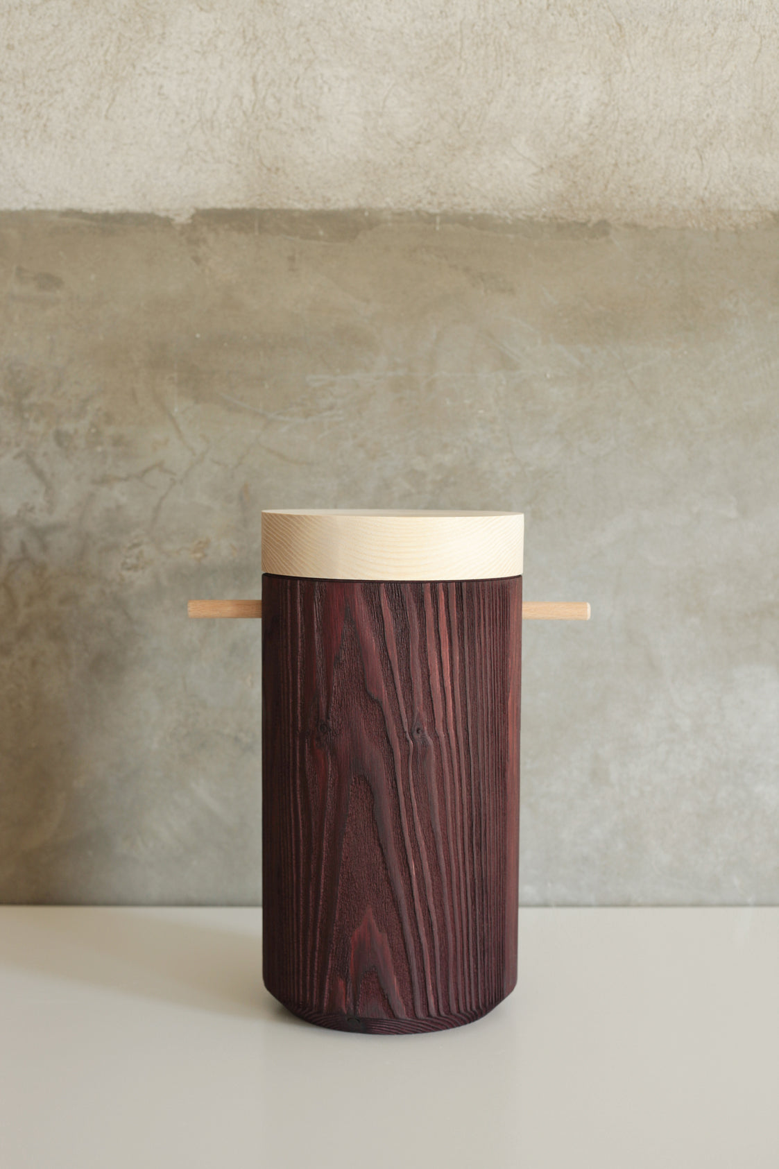 Cylinder shaped, brown wooden urn displayd on a white able